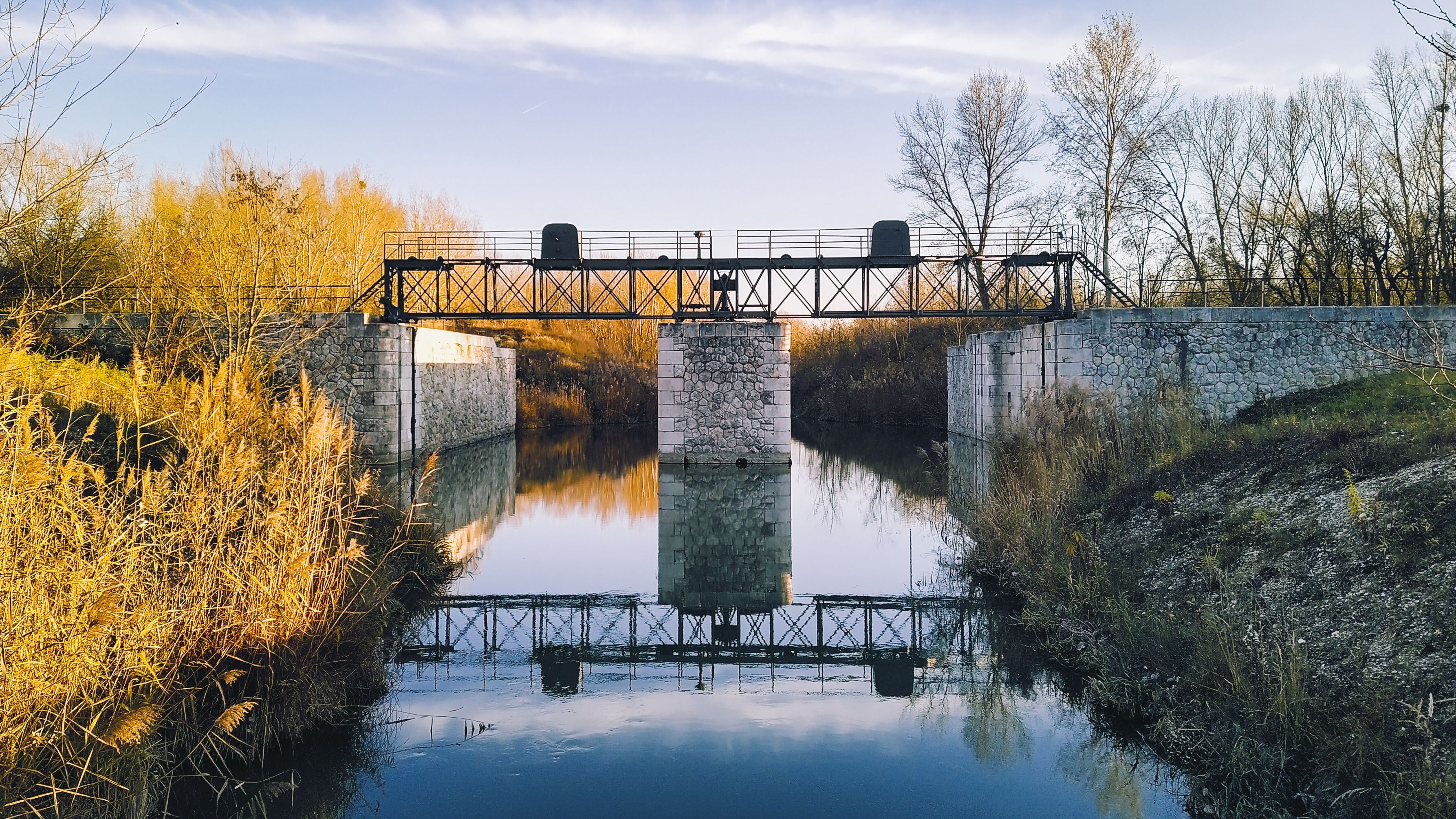 Ein Schloss mit Steinmauer und schmiedeeisernen Toren, umgeben von Wasser und Bäumen.