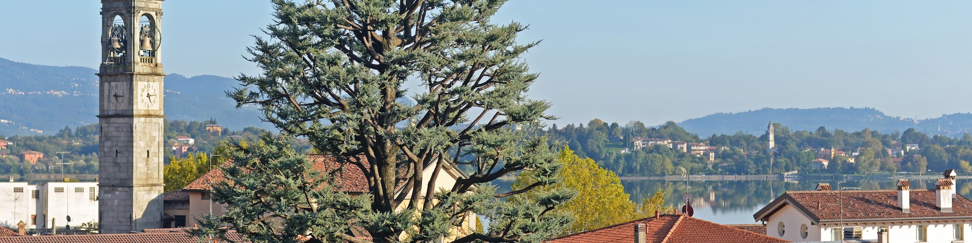 Church with bell tower, houses and trees in Pusiano with view on the hills and the lake in the back at Lago di Pusiano in Lombardy, Brianza area, Italy