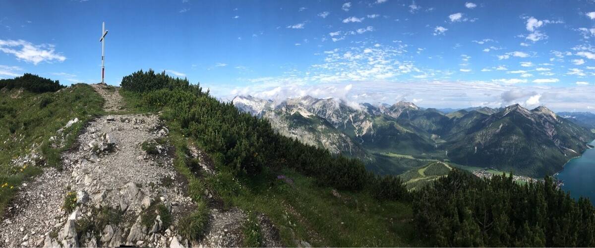 A mountain trail with a weather station, a lake, and surrounding peaks.