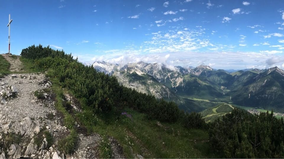 A mountain trail with a weather station, a lake, and surrounding peaks.