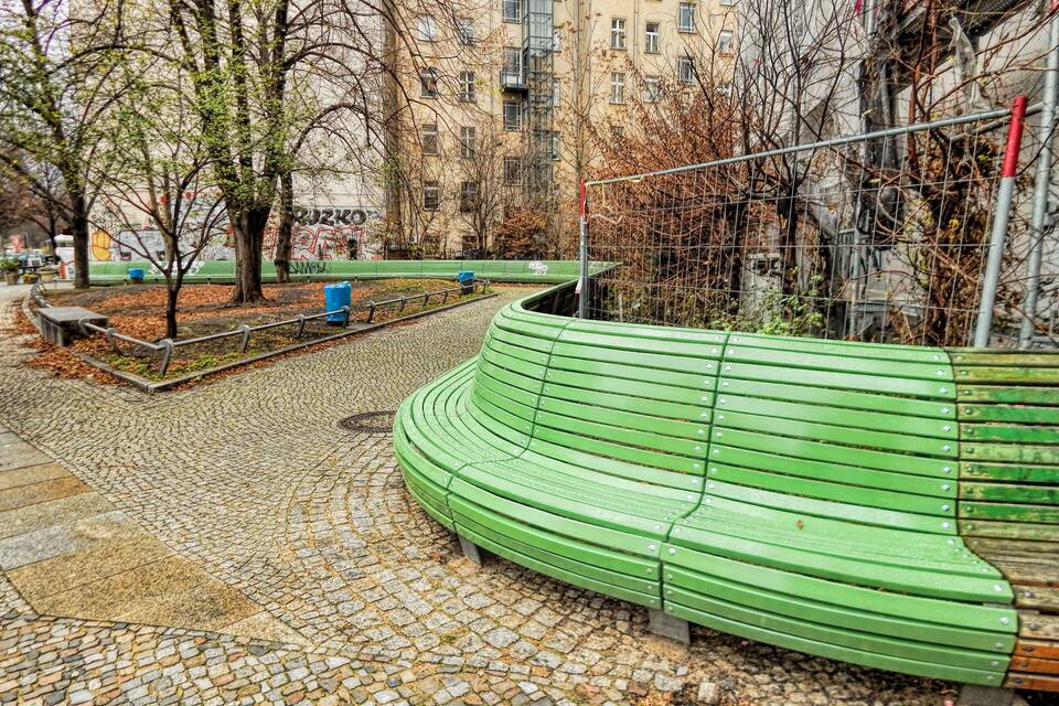 Um banco verde em um parque com caminhos de pedra e árvores sem folhas.