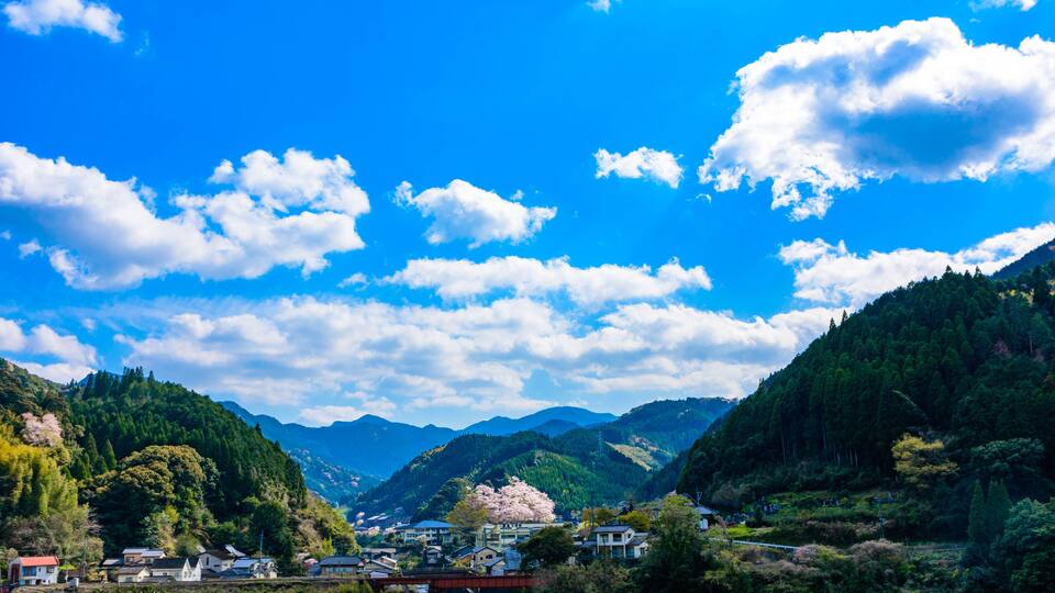 A mountainous landscape with a river, houses, and a bridge.
