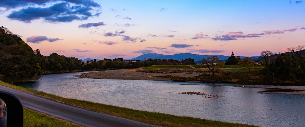 A river winding through a landscape with mountains in the distance and a road alongside.