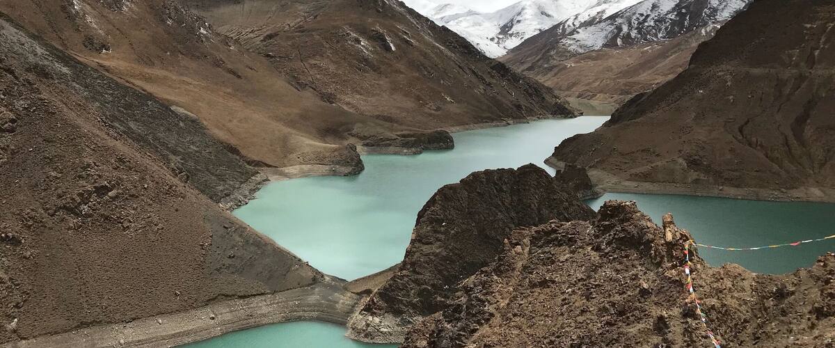 A turquoise lake surrounded by rugged mountains with snow-capped peaks.