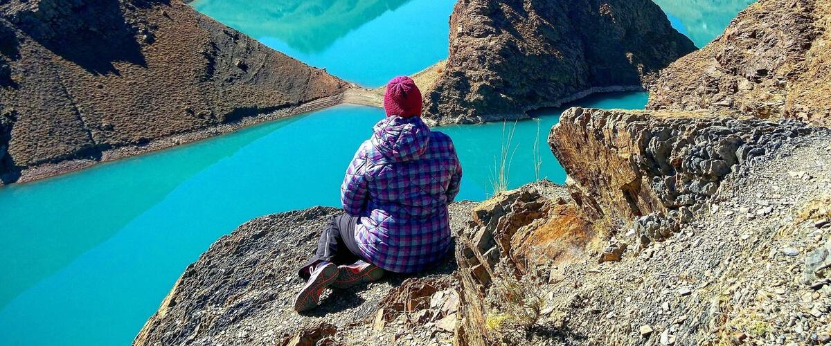 A person sitting on a rocky outcrop overlooking a turquoise lake surrounded by mountains.