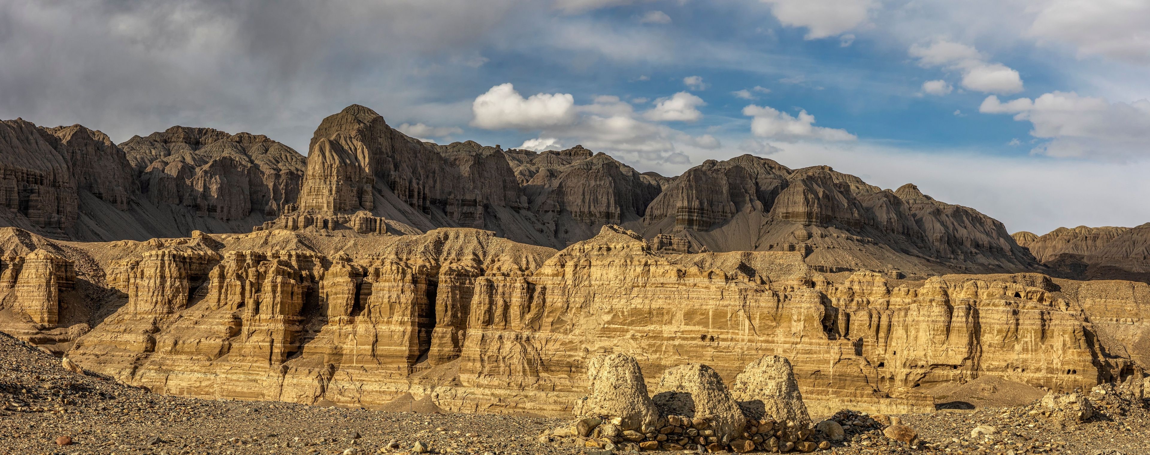 Eine zerklüftete Berglandschaft mit schichtartigen Felsformationen und blauem Himmel.