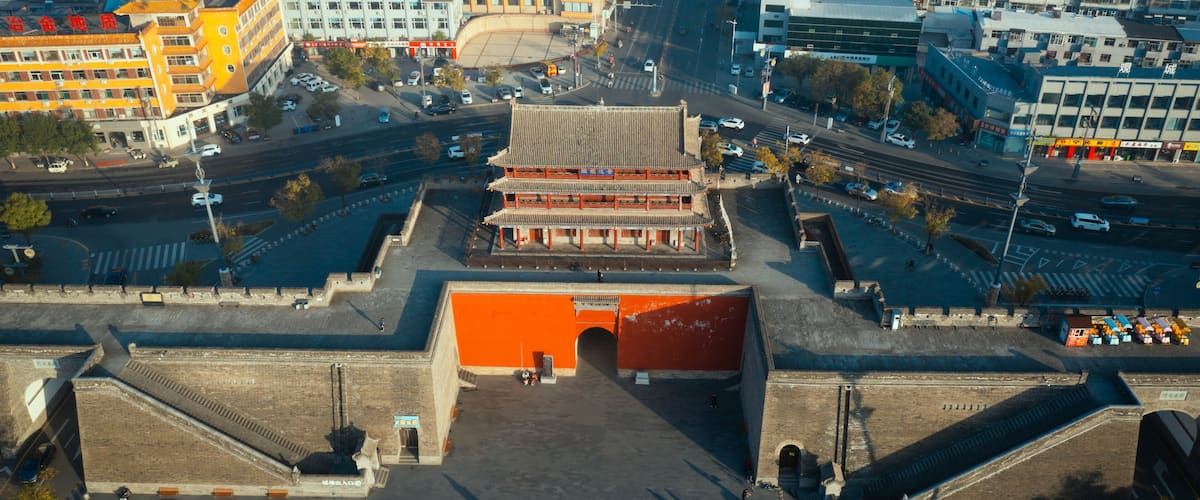 An aerial view of a city with traditional architecture, a prominent red gate, and modern buildings.