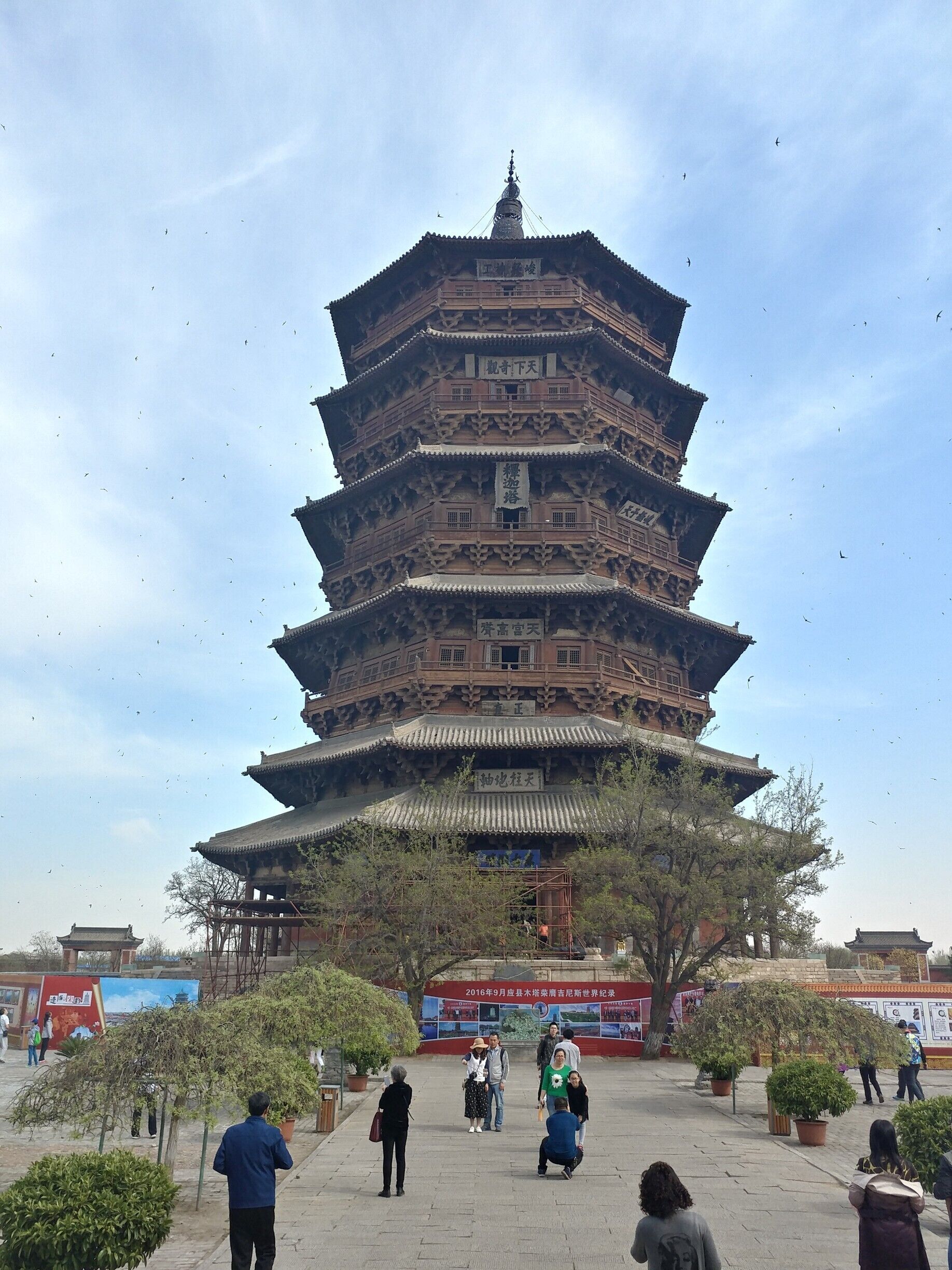 A multi-tiered pagoda with traditional architecture, surrounded by a paved area with potted plants and people.
