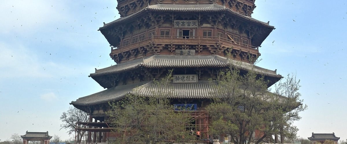A multi-tiered pagoda with traditional architecture, surrounded by a paved area with potted plants and people.
