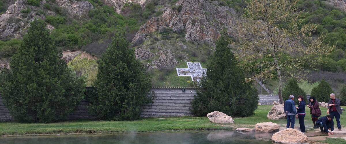 A clear lake with rocky mountains in the background and a cross-shaped structure in the water.