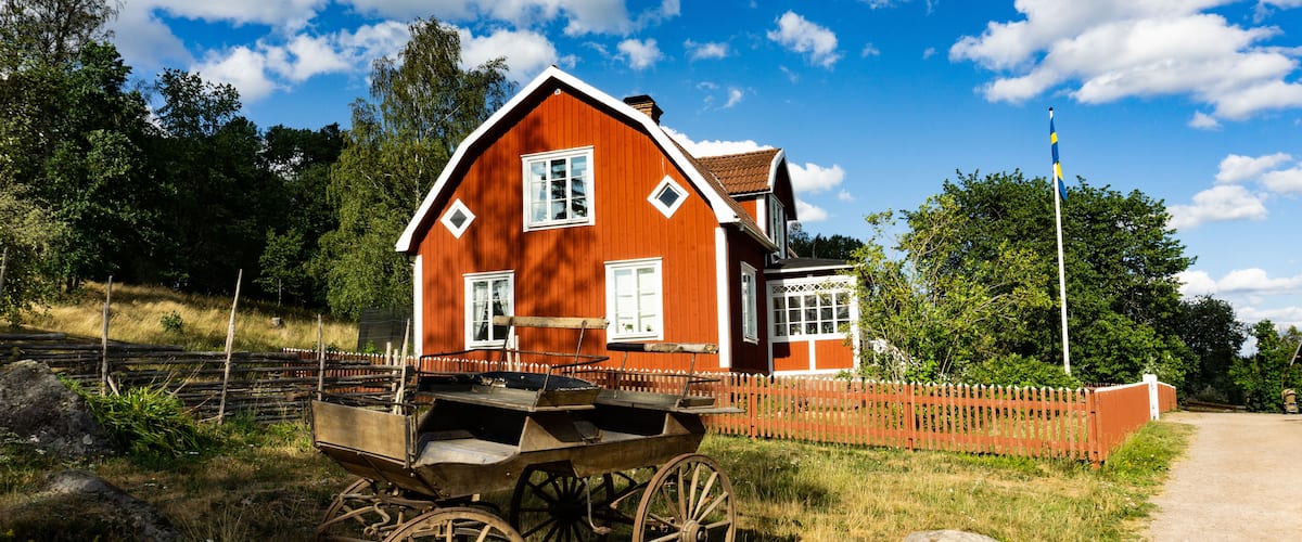 A red wooden house with white trim, a wooden cart, and a wooden fence.