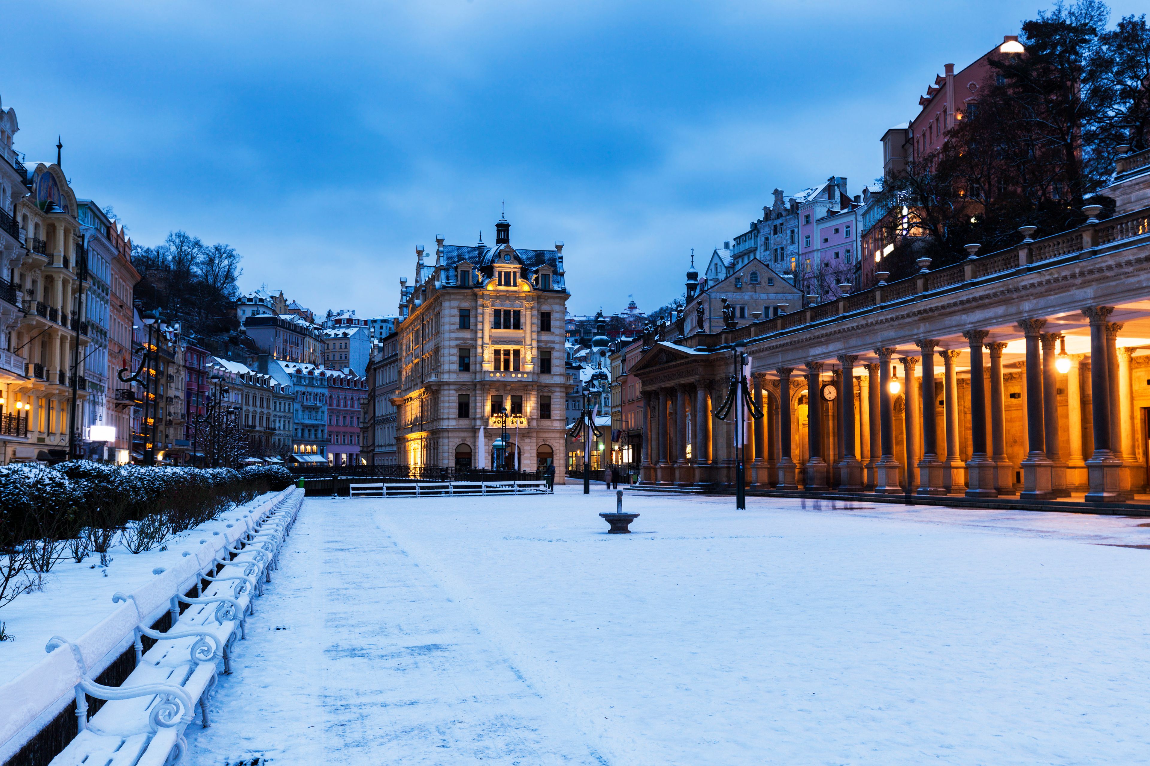 A snow-covered square with ornate buildings and a fountain.