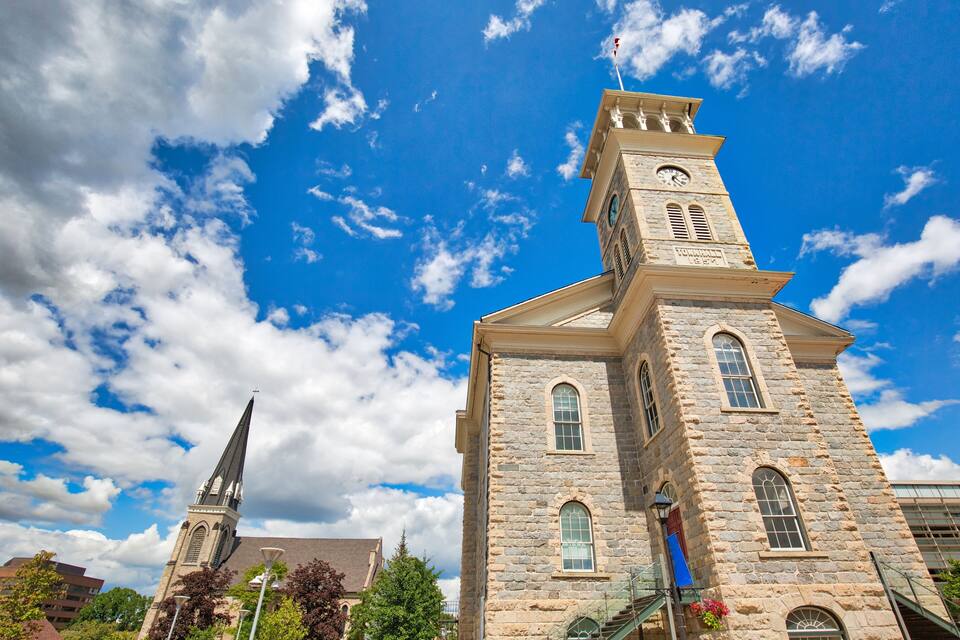 A historic stone building with a clock tower and a steeple under a blue sky with clouds.