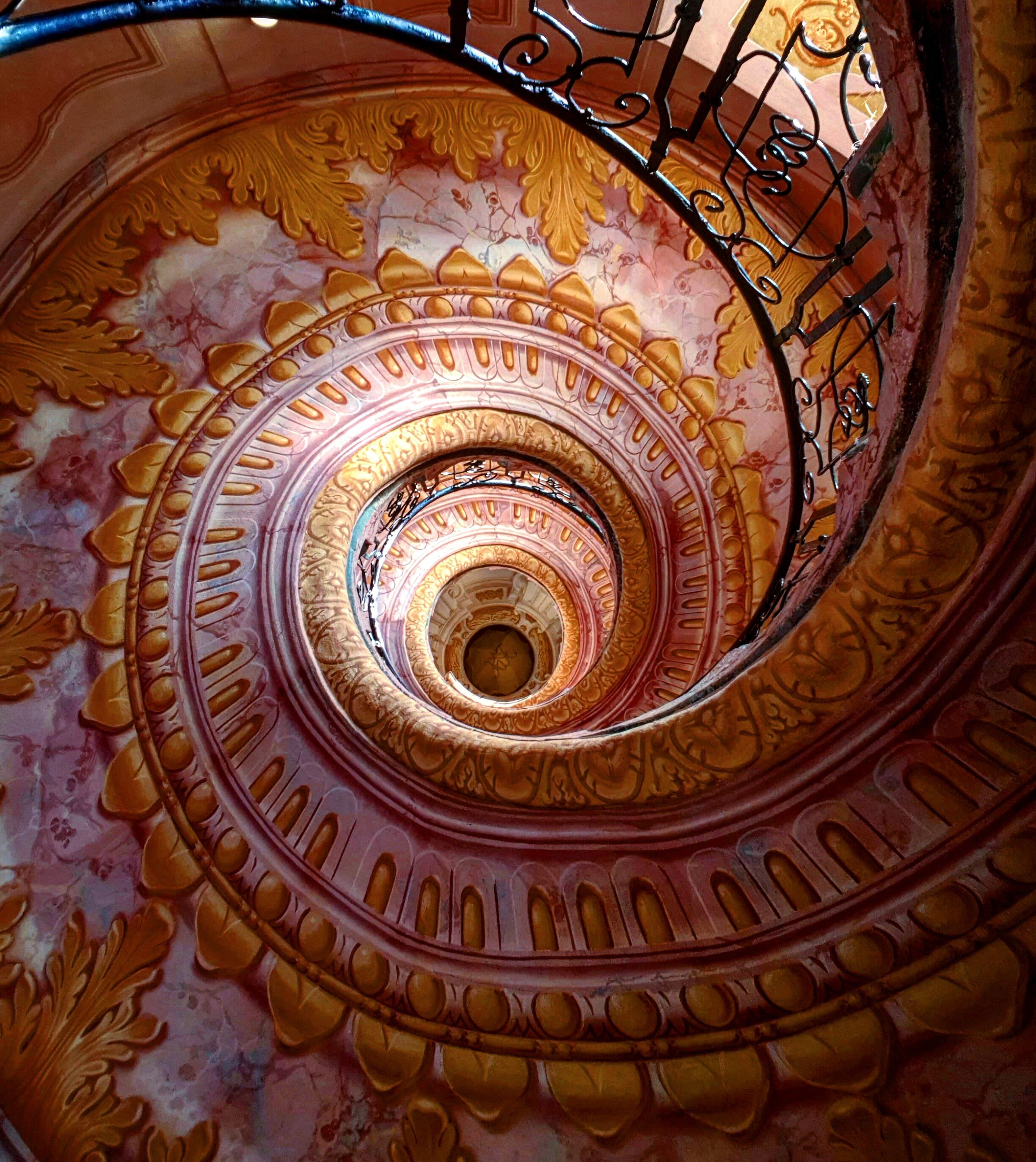 A spiral staircase with ornate golden and pink floral patterns.