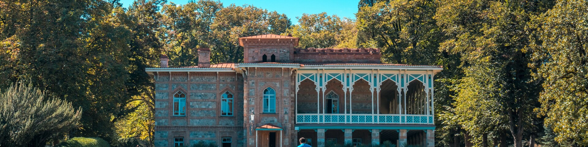 Um edifício histórico com telhado em azulejos, rodeado por um gramado bem cuidado e árvores.