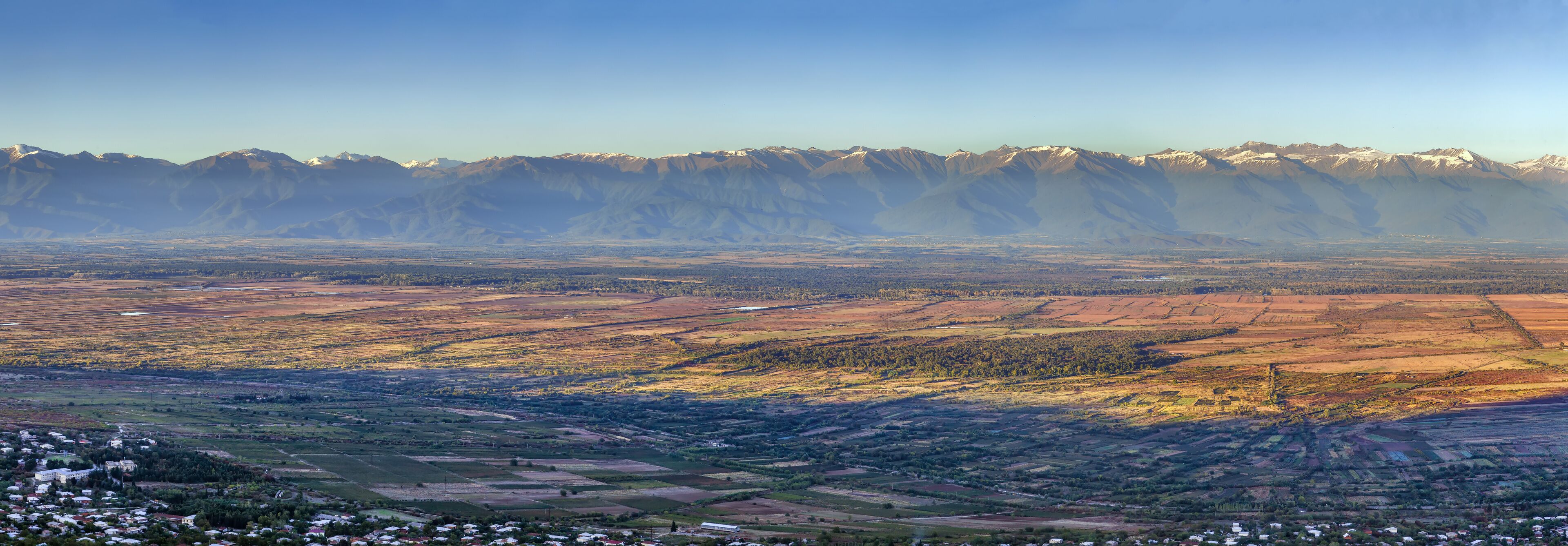 A mountainous landscape with snow-capped peaks, terraced fields, and a small settlement.