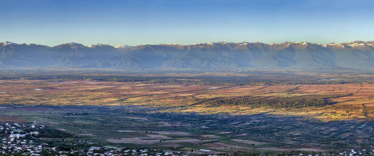 A mountainous landscape with snow-capped peaks, terraced fields, and a small settlement.