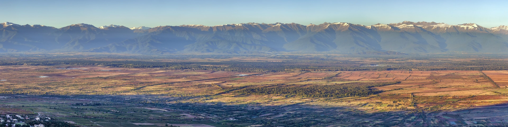 A mountainous landscape with snow-capped peaks, terraced fields, and a small settlement.