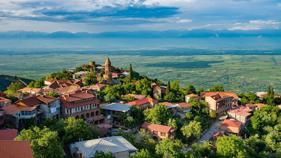 A village with historic architecture, a prominent church, and a mountainous backdrop.