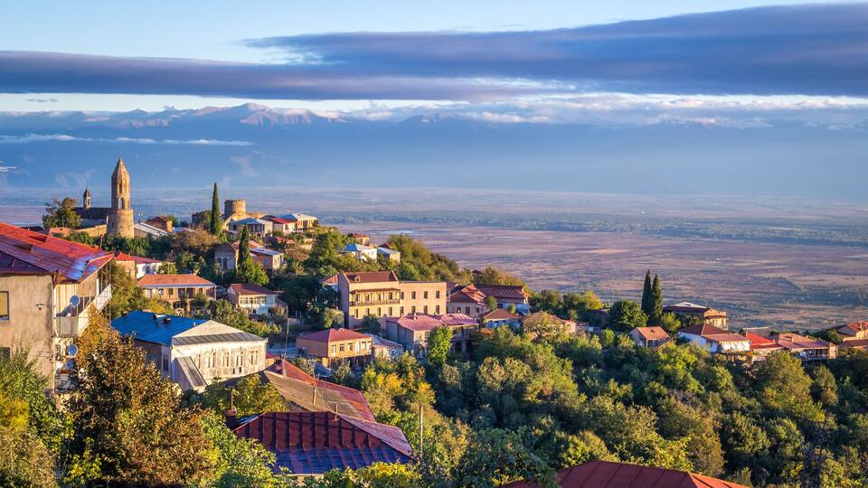 A town with historic architecture, a prominent tower, and a mountainous backdrop.