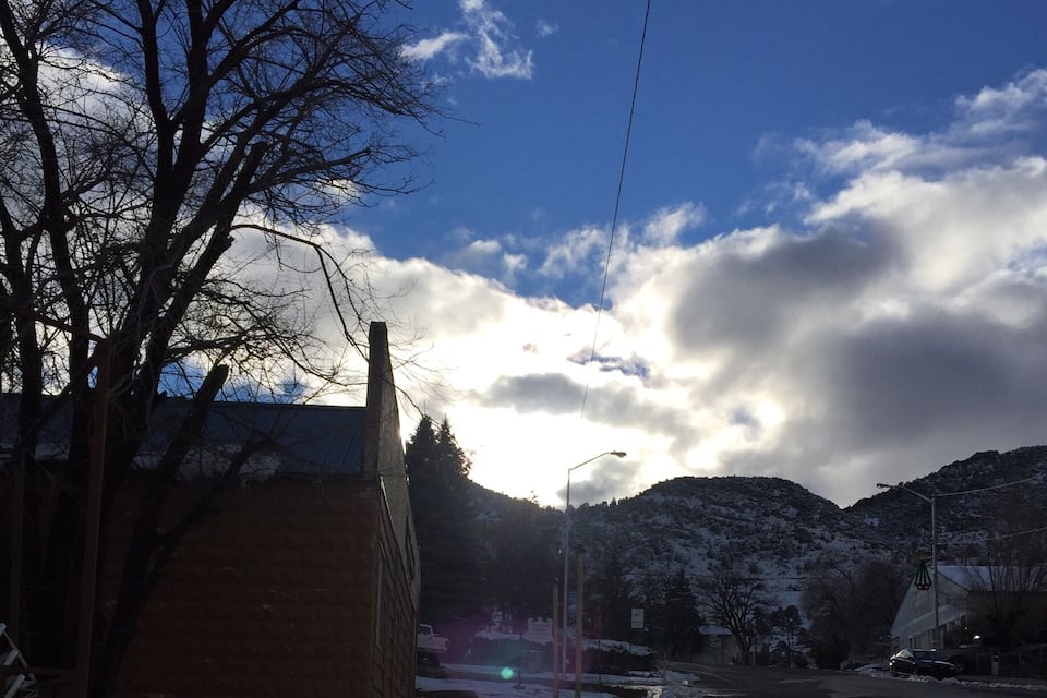 A snowy sidewalk with a tree and a building on the left, a streetlight, and a mountain in the background.