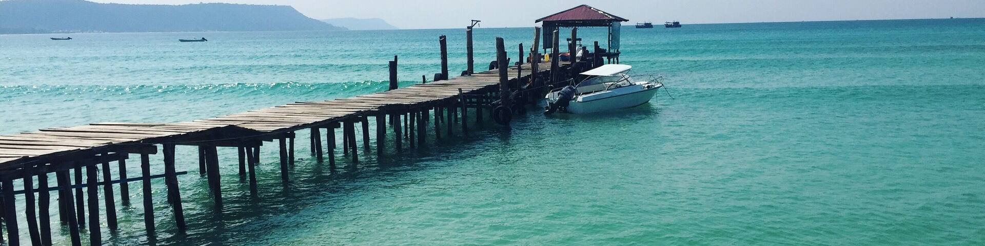 Un muelle de madera que se adentra en aguas turquesas, con una pequeña embarcación amarrada al final.