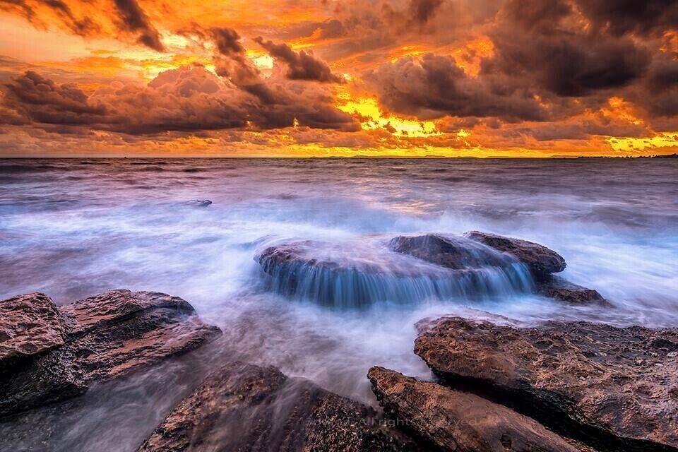 A rocky shoreline with a waterfall and a sunset over the ocean.