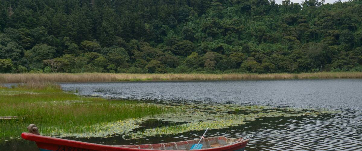 A small blue boat with red trim, labeled "ZAPASSA," docked by a calm lake with dense forest in the background.