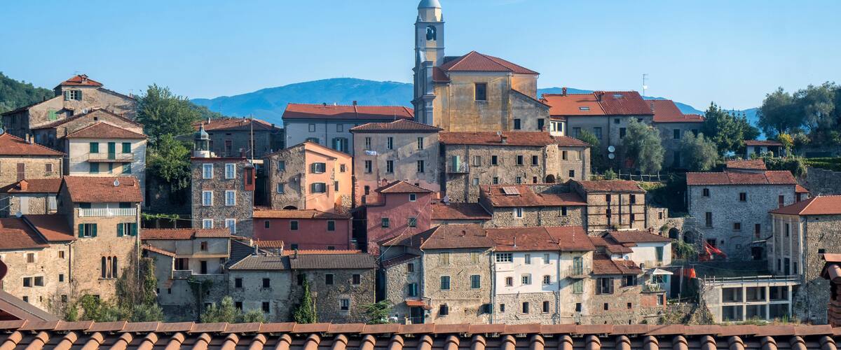 A historic town with stone buildings, a prominent church with a bell tower, and a mountain in the background.