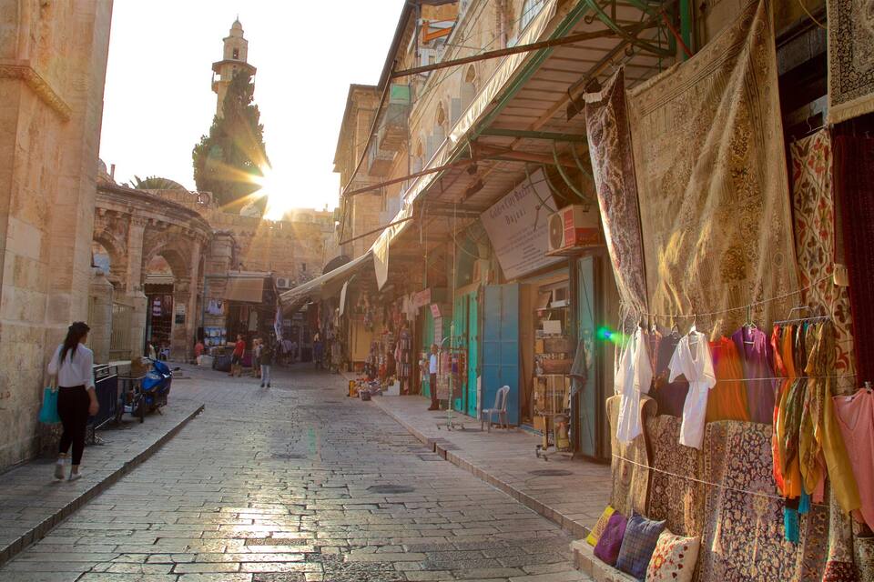 Una calle soleada con comercios y una mezquita al fondo.