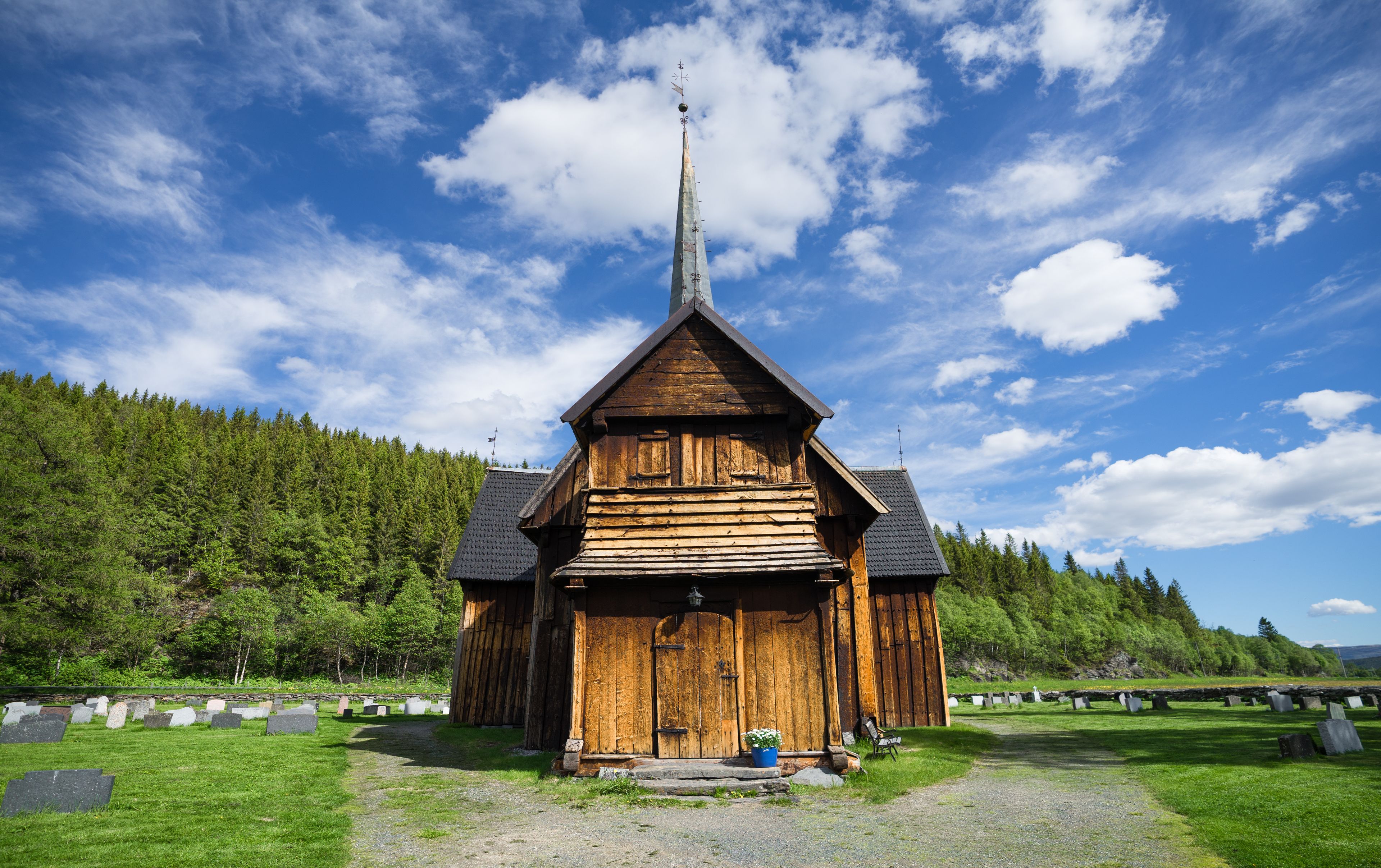 Una iglesia de madera con un campanario alto, rodeada por un cementerio con lápidas.