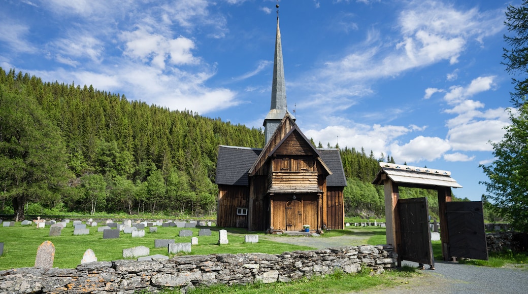 Une église en bois, dotée d’un clocher imposant, entourée d’un cimetière où se trouvent des pierres tombales et un mur de pierre.