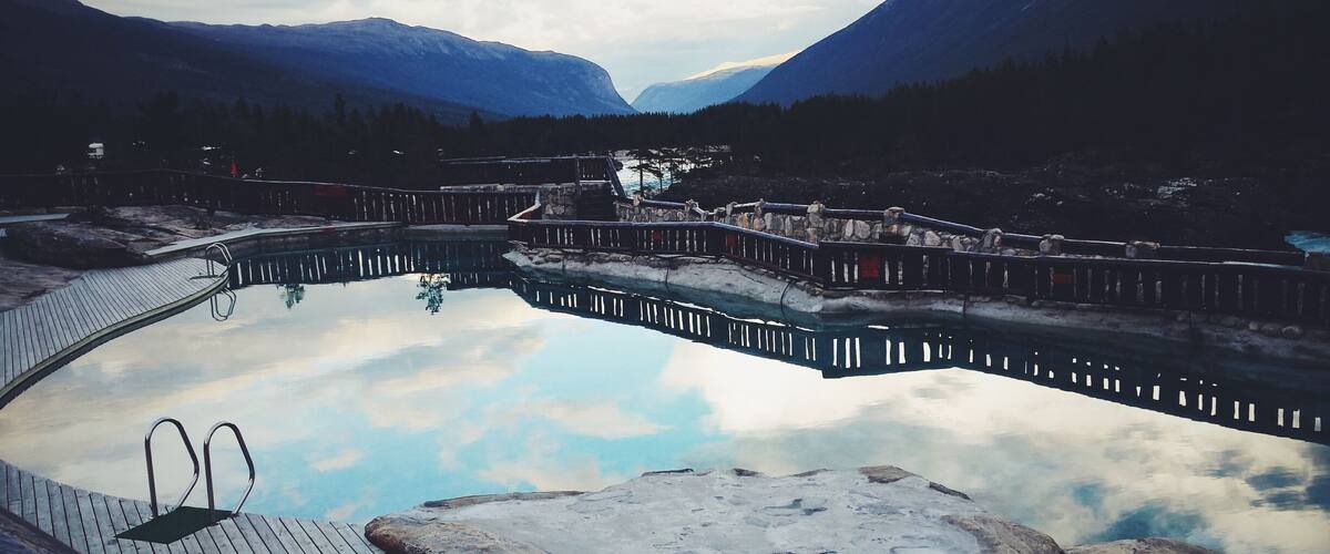 A natural hot spring surrounded by mountains and a wooden deck.