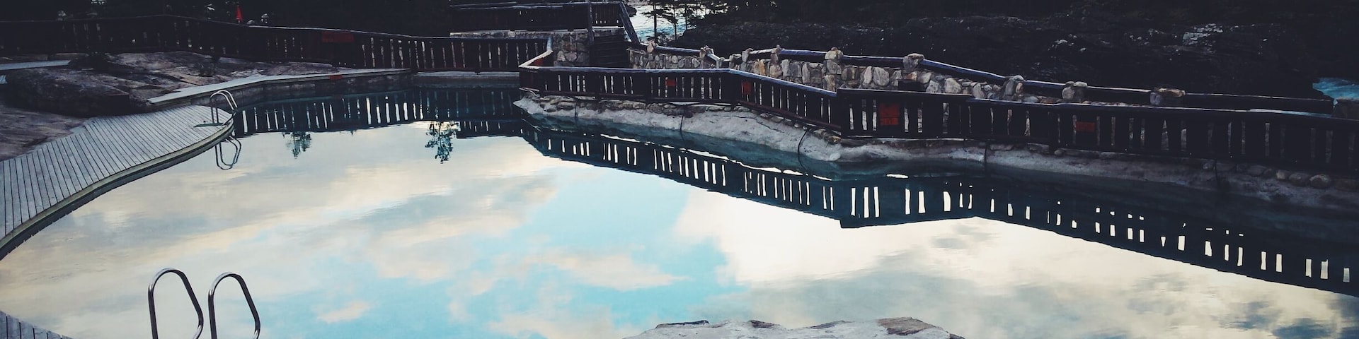 A natural hot spring surrounded by mountains and a wooden deck.