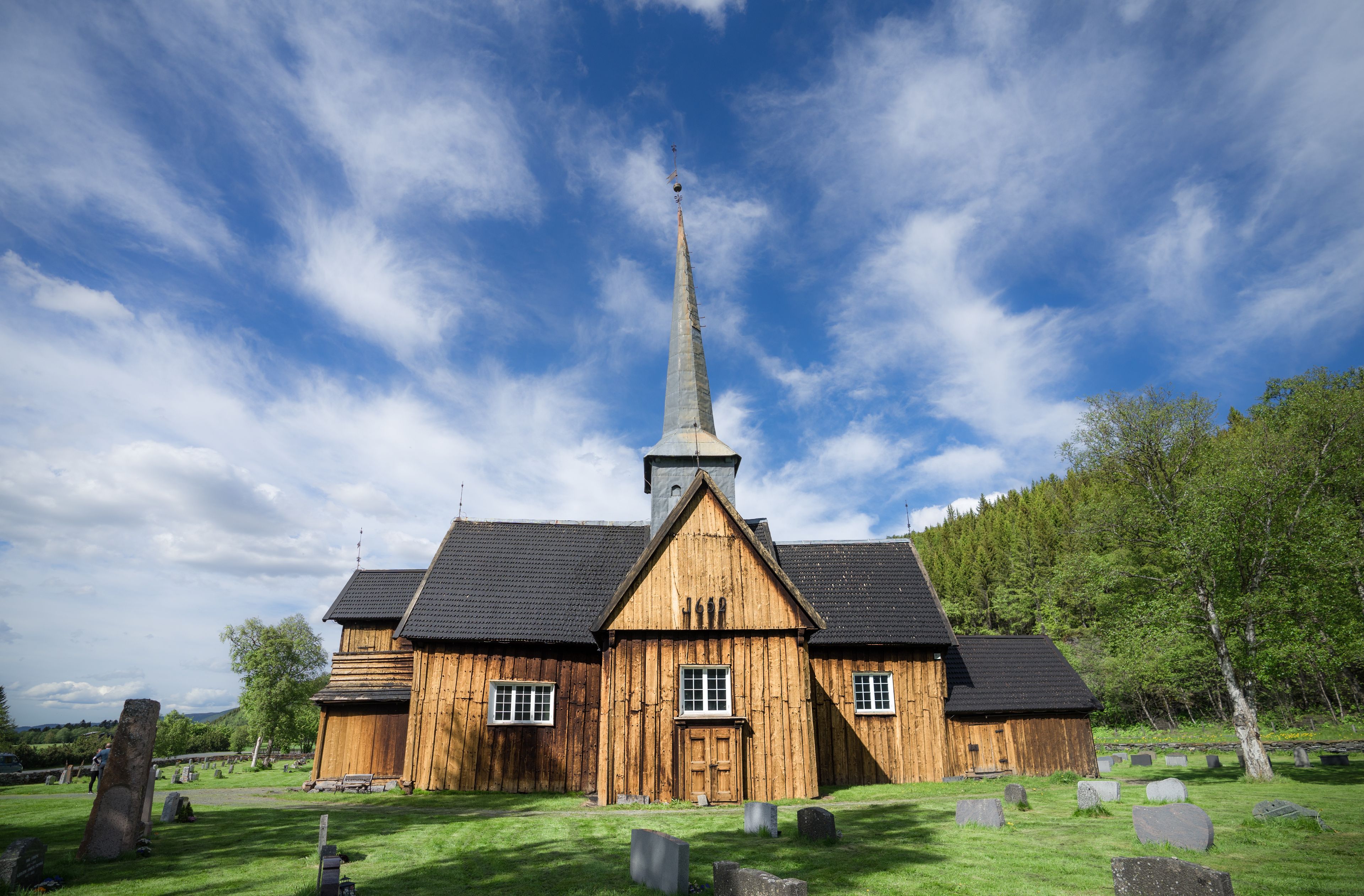 Une église en bois, dotée d’un clocher imposant, avec un cimetière en premier plan.