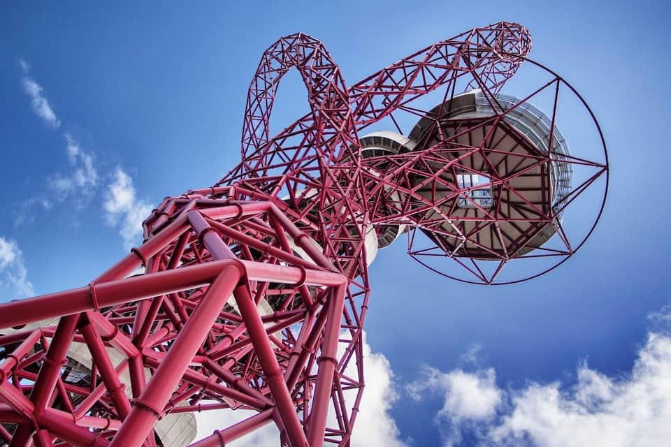 Eine große, rote Metallkonstruktion mit einer kreisförmigen Aussichtsplattform vor blauem Himmel mit Wolken.