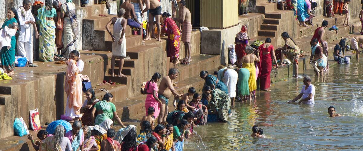 A crowded riverbank with people bathing and socializing.