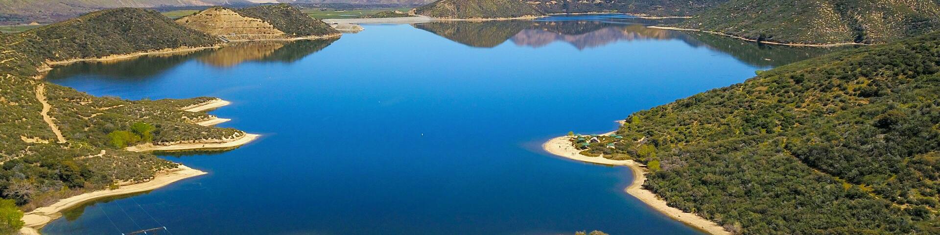 a majestic aerial panoramic shot of the vast blue still lake water with breathtaking mountain ranges reflecting off the lake with a rainbow at Silverwood Lake in Hesperia California USA