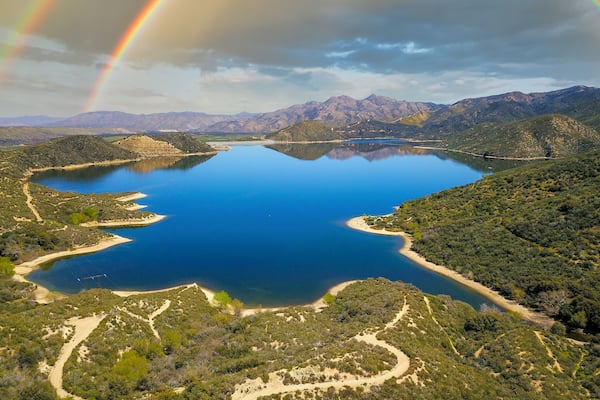 a majestic aerial panoramic shot of the vast blue still lake water with breathtaking mountain ranges reflecting off the lake with a rainbow at Silverwood Lake in Hesperia California USA
