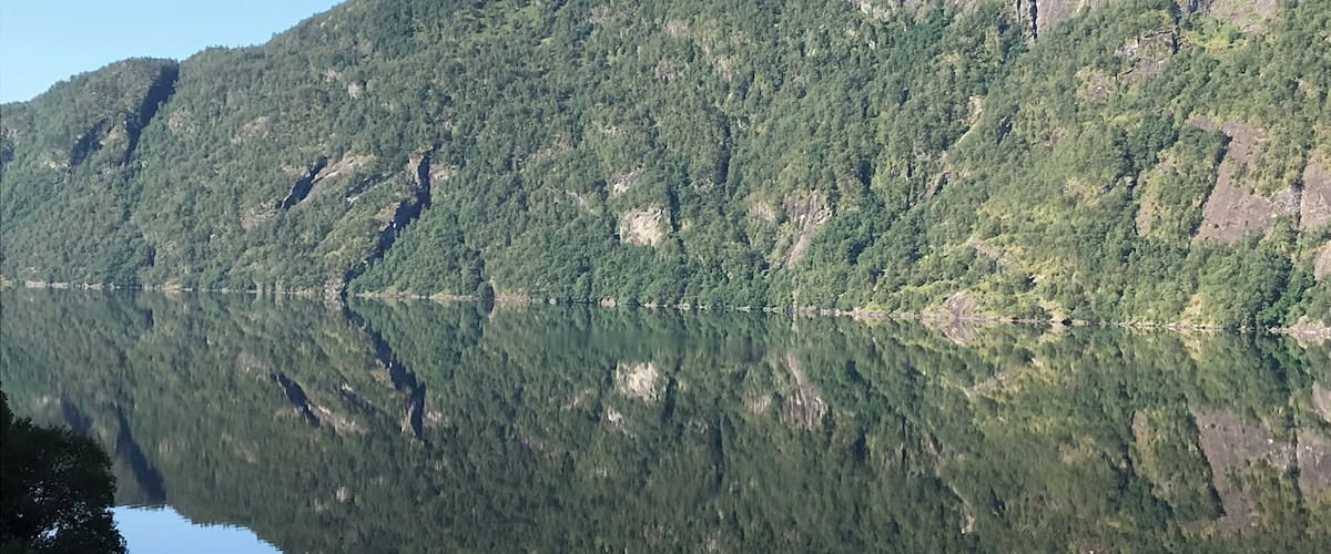 A calm lake reflecting a forested mountain range.
