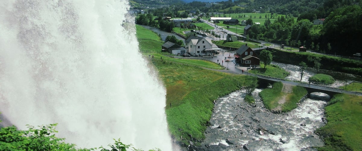 A waterfall cascading down a rocky cliff, a river flowing through a valley, and a small village with houses and a bridge.