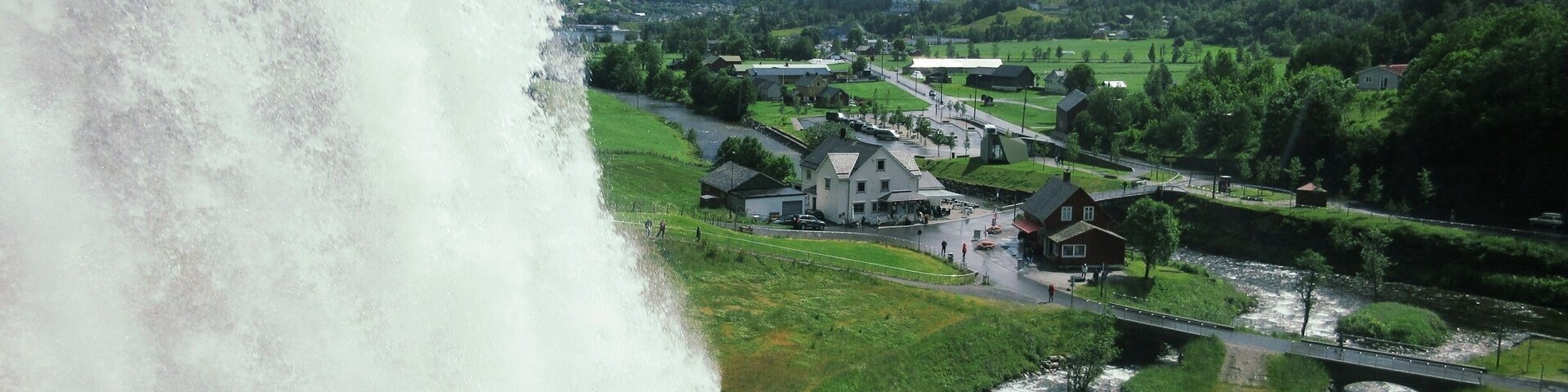 A waterfall cascading down a rocky cliff, a river flowing through a valley, and a small village with houses and a bridge.
