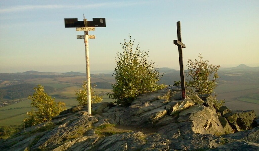 A rocky hilltop with a wooden cross and a directional signpost.