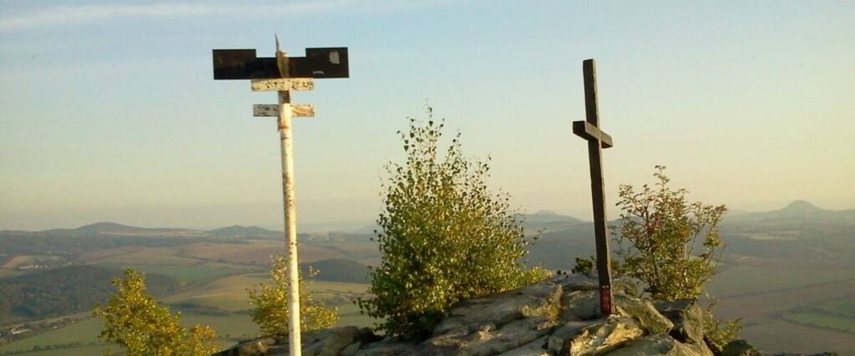A rocky hilltop with a wooden cross and a directional signpost.