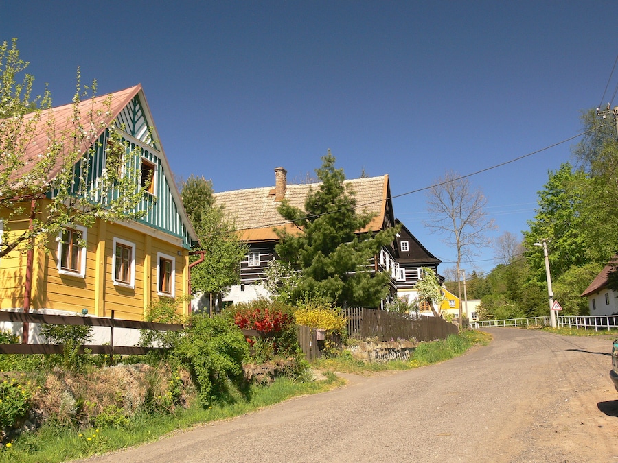 Un camino rural con casas coloridas, una valla de madera y un cielo azul despejado.