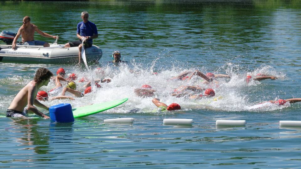 A group of swimmers in a lake with a boat and buoys in the water.