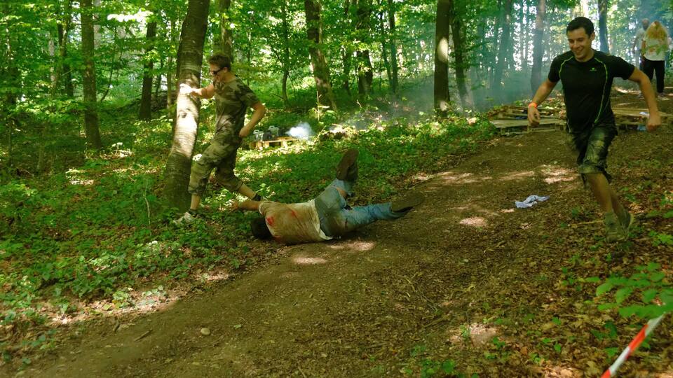 A forested area with a dirt path, a person lying on the ground, and another person running.