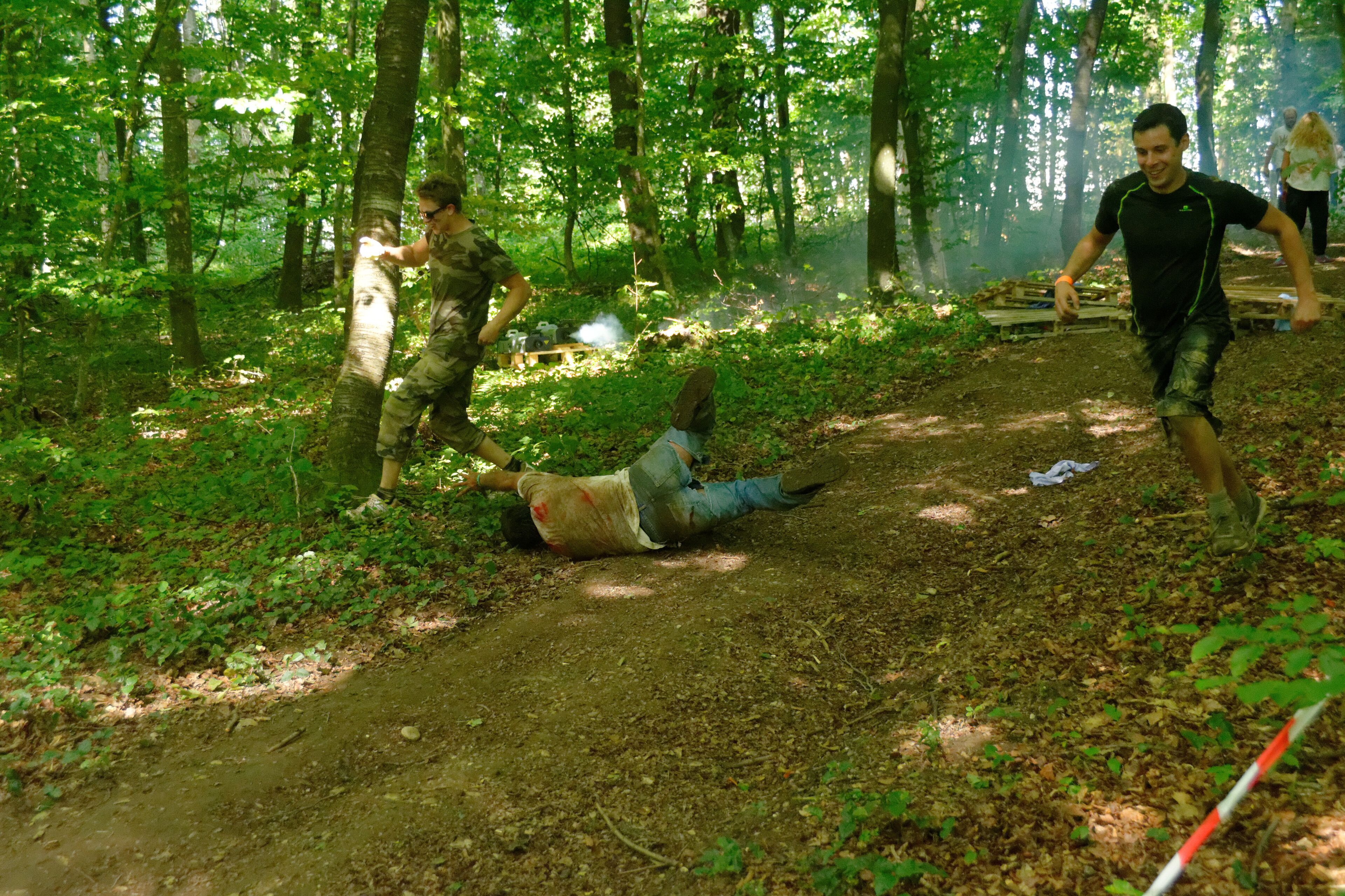 A forested area with a dirt path, a person lying on the ground, and another person running.