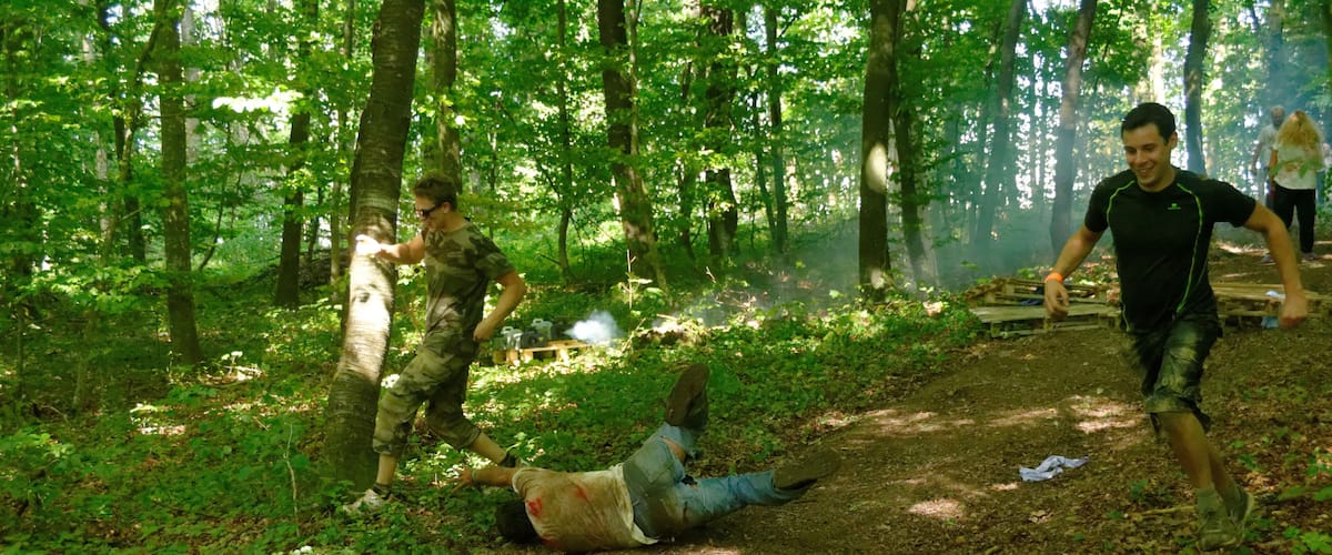 A forested area with a dirt path, a person lying on the ground, and another person running.