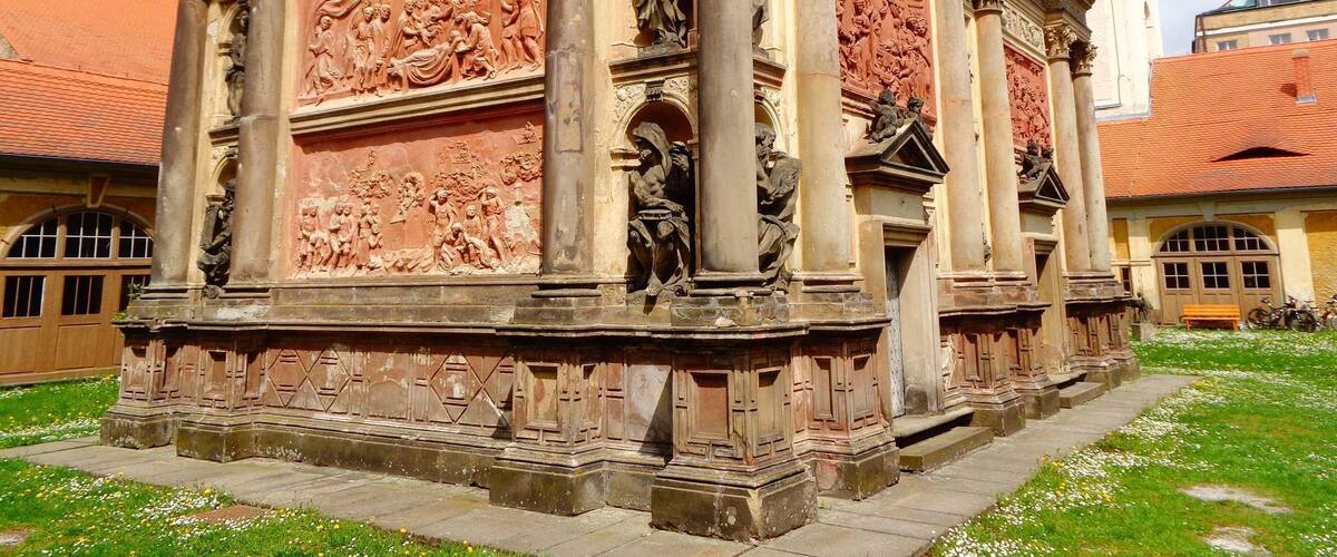 A historical building with intricate carvings and columns, surrounded by a grassy area and other buildings.